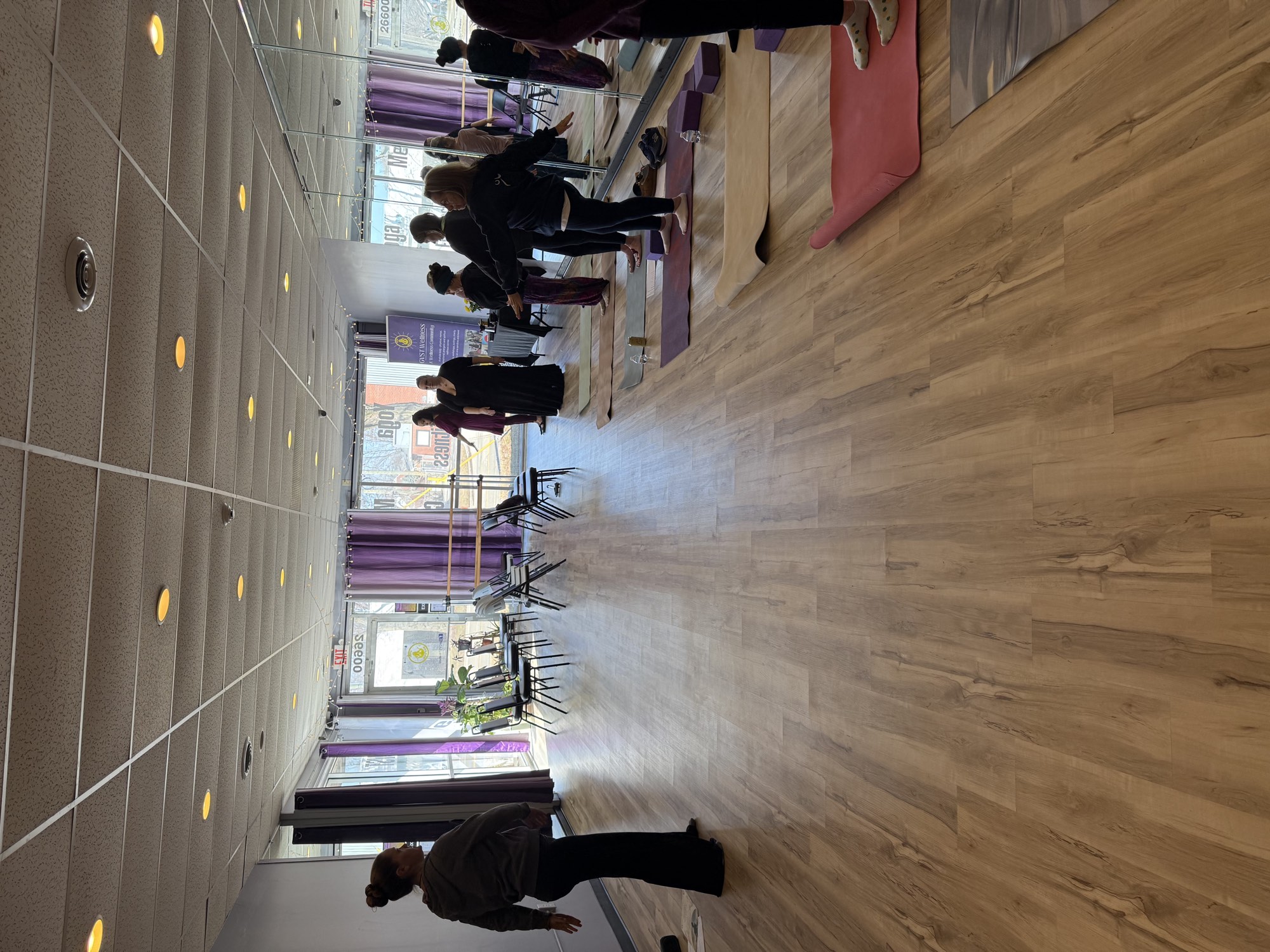 A full yoga class mid-practice at GVST Wellness in St. Clair Shores, arms raised on mats in the studio
